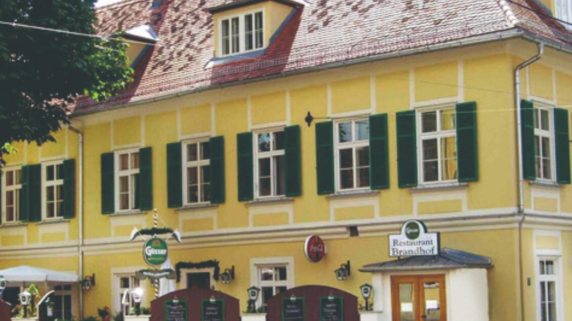Ein charmantes, gelbes Gebäude mit grünen Fensterläden. Das Haus beherbergt ein Restaurant und hat eine einladende Atmosphäre. | © Brandhof