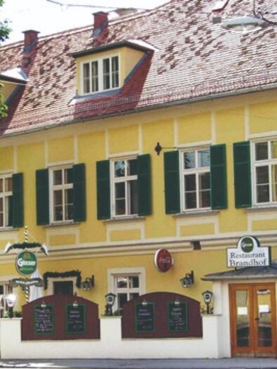 Ein charmantes, gelbes Gebäude mit grünen Fensterläden. Das Haus beherbergt ein Restaurant und hat eine einladende Atmosphäre. | © Brandhof