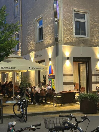 Exterior view of the Demiri café-restaurant at night with illuminated entrance area and guests. | © Demiri