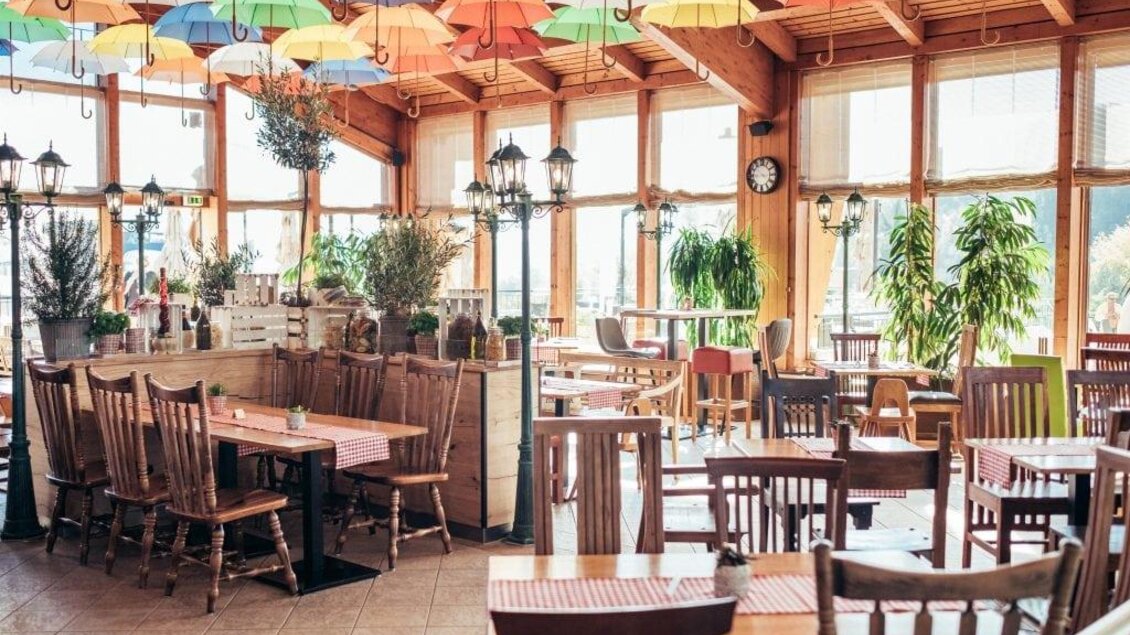Ein gemütliches Restaurant mit Holztischen und Stühlen. Bunte Regenschirme hängen von der Decke und schaffen eine einladende Atmosphäre. | © Thermenresort Loipersdorf