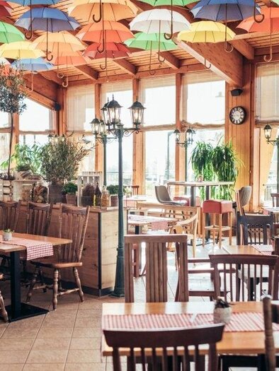 A cozy restaurant with wooden tables and chairs.  
Colorful umbrellas hang from the ceiling, creating an inviting atmosphere. | © Thermenresort Loipersdorf
