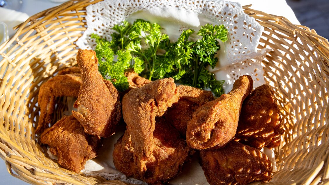 Ein Korb mit goldbraunem, frittiertem Hähnchen und frischen Kräutern. Das Essen sieht lecker und einladend aus. | © Lipizzanerheimat-Schiffer