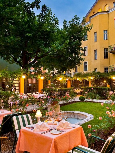 A beautiful garden with tables and chairs, festively decorated. Flowers are blooming around the tables and there is gentle lighting. | © Graz Tourismus - Werner Krug