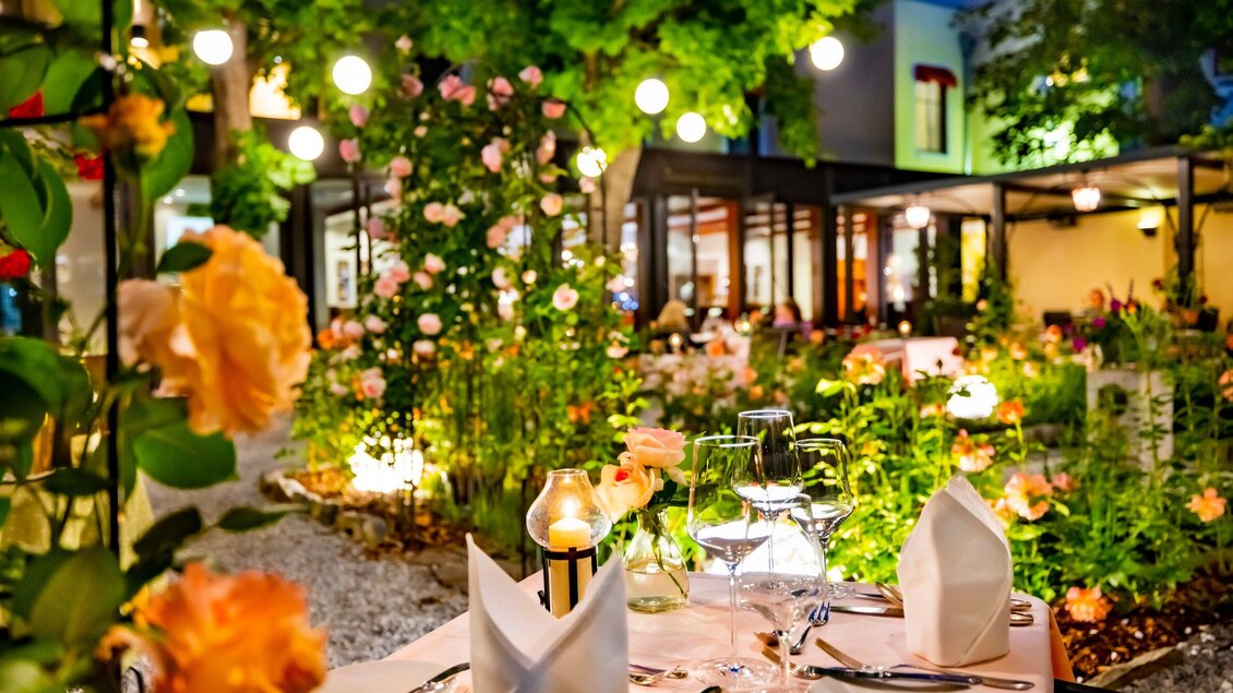Ein wunderschöner Garten mit vielen Blumen und laternenbeleuchtetem Ambiente. Der Tisch ist elegant gedeckt und lädt zum Essen ein. | © Das Florian