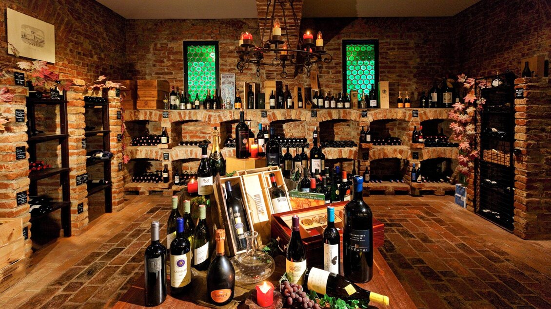 Ein gemütlicher Weinkeller mit Regalen voller Weinflaschen. Die Wände sind aus Ziegelstein, und es gibt dekorative Details wie Kerzen und Pflanzen. | © Das Florian - Werner Krug