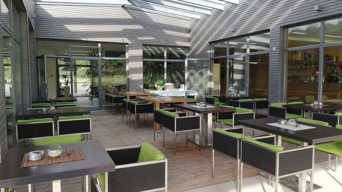 Ein modernes Restaurant mit hellen, offenen Räumen und großen Fenstern. Tische mit schwarzen und grünen Stühlen laden zum Verweilen ein. | © Restaurant - Bistro Golfblick