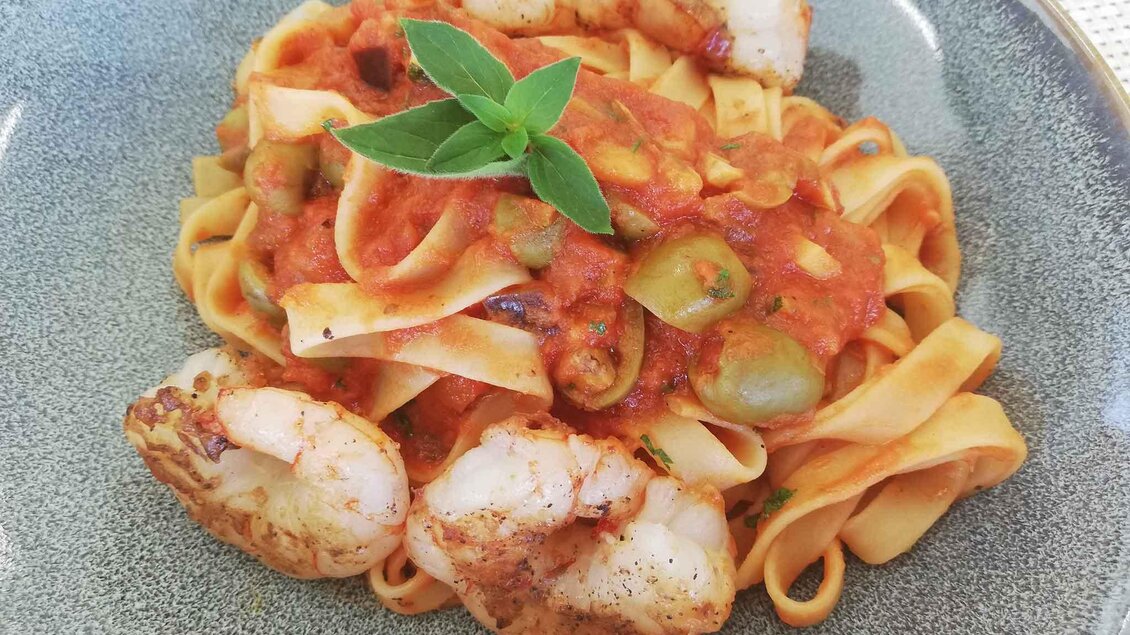 Ein Teller mit Bandnudeln, garniert mit Garnelen und einer Tomatensoße. Frische Kräuter verleihen dem Gericht einen geschmackvollen Akzent. | © Restaurant - Bistro Golfblick