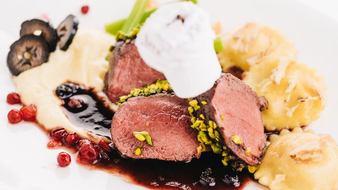 Ein elegantes Gericht mit zartem Fleisch, dekoriert mit Pistazien und einer kreativen Sauce. Dazu Ravioli und eine Beilage aus püriertem Gemüse.
