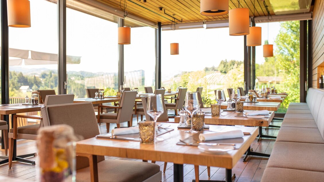 Ein modernes Restaurant mit großen Fenstern und Blick auf die Natur. Die Tische sind schön gedeckt und die Beleuchtung ist warm und einladend. | © Regionalmanagement Südweststeiermark GmbH/webquart