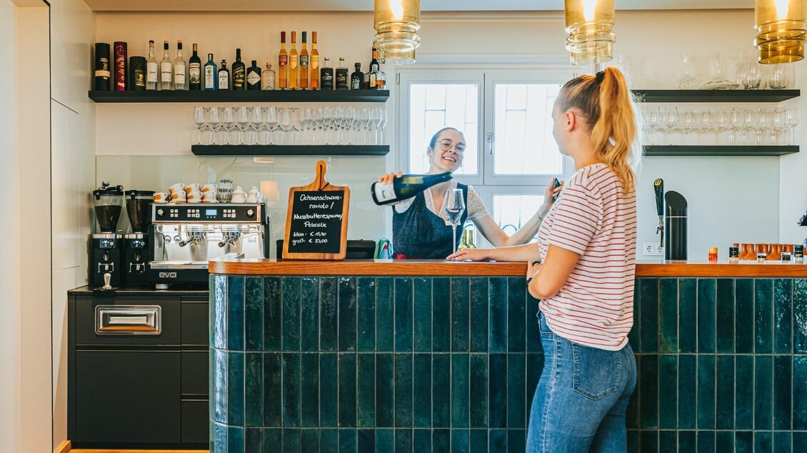 Eine freundliche Bedienung schenkt einem Gast ein Getränk an der Bar. Der Raum ist hell und modern gestaltet. | © Regionalmanagement Südweststeiermark GmbH/webquartier