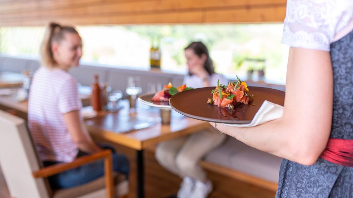 Eine Kellnerin serviert Teller mit köstlichen Speisen. Im Hintergrund sitzen zwei Gäste in einem modernen Restaurant. | © Regionalmanagement Südweststeiermark GmbH/webquartier