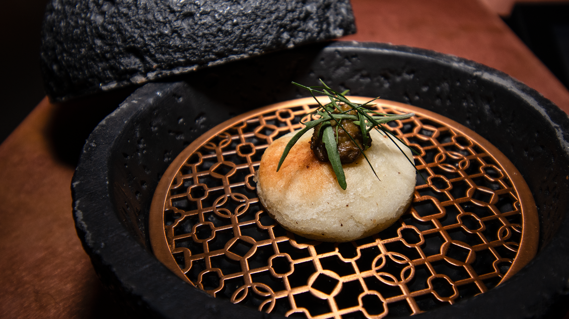 Ein zartes Bao-Brötchen mit einer Garnitur aus frischen Kräutern, serviert in einem stilvollen Dampfer. Die Präsentation kombiniert moderne Ästhetik und kulinarische Kunst. | © Kupferdachl - Heidi Edelsbrunner