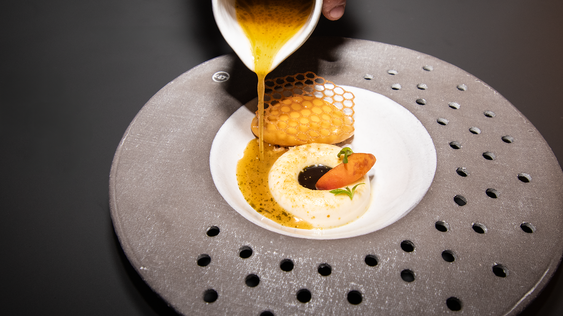 Eine geschmackvolle Speise wird serviert. Eine goldene Flüssigkeit wird über eine elegante Präsentation aus Creme und einem knusprigen Element gegossen. | © Kupferdachl - Heidi Edelsbrunner
