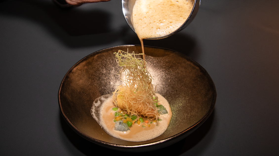 Eine handgelauschte Suppe wird in eine Schüssel gegossen. Das Gericht wird von einer knusprigen Garnitur begleitet. | © Kupferdachl - Heidi Edelsbrunner