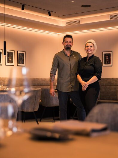 A modern restaurant with stylish design. Two people are smiling in the foreground. | © Nadine Geuter- Black Ink Production