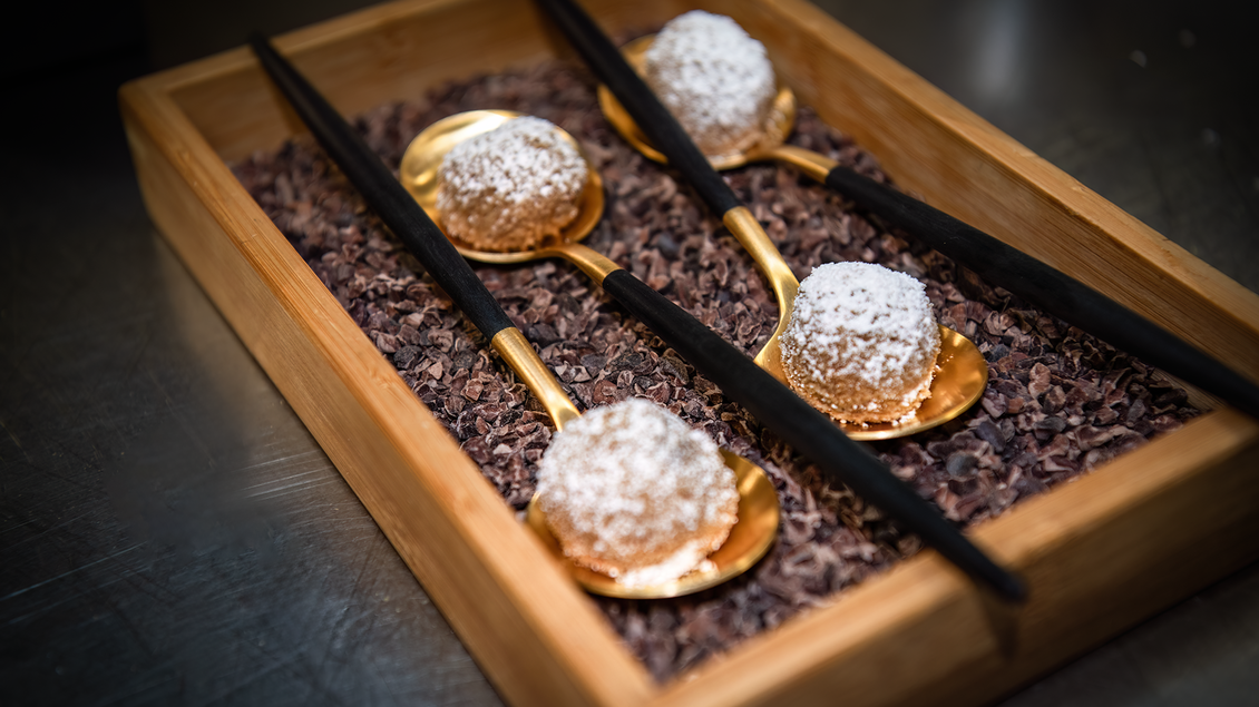 Eine elegante Präsentation von vier Delikatessen in einer Holzkiste. Die Leckereien sind auf goldenen Löffeln angerichtet und mit Puderzucker bestäubt. | © Kupferdachl - Heidi Edelsbrunner
