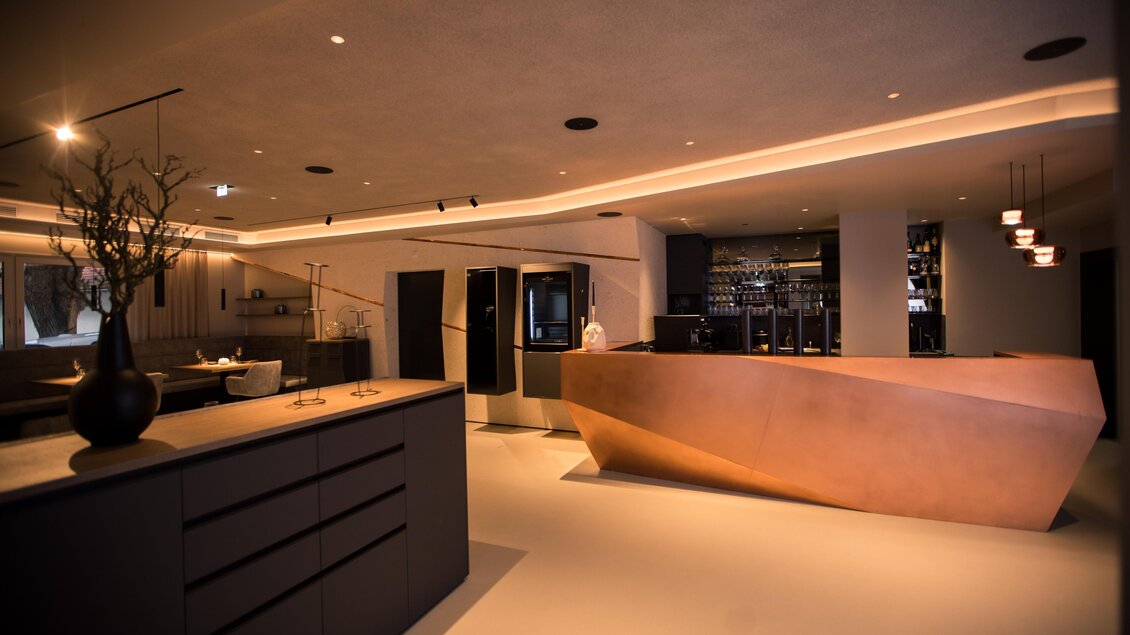 Ein modernes Innendesign mit einer eleganten Empfangstheke und stilvollen Möbeln. Die Beleuchtung sorgt für eine gemütliche Atmosphäre. | © Kupferdachl - Black Ink Production