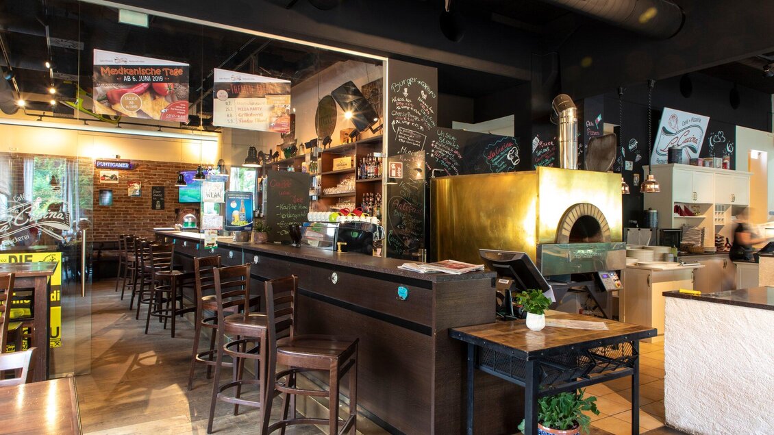Ein gemütliches Restaurant mit einer Bar und Holzstühlen. Im Hintergrund befindet sich ein Pizzaofen und eine einladende Atmosphäre. | © TV Region Graz - Lunghammer