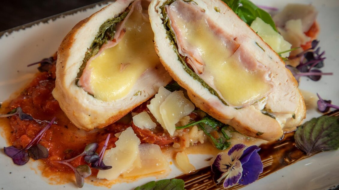 Ein köstliches Gericht mit gefülltem Hähnchenbrustfilet, das mit Schinken und Käse gefüllt ist. Es liegt auf einer bunten Gemüsesauce, verziert mit essbaren Blüten. | © TV Region Graz - Lunghammer