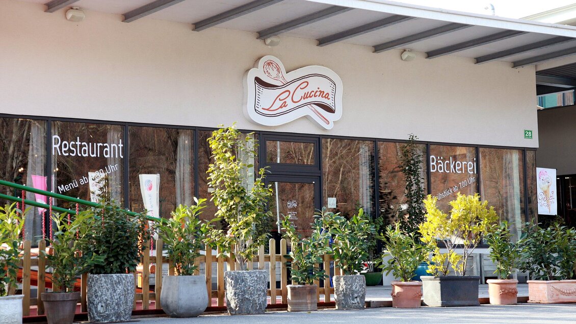 Ein einladendes Restaurant mit dem Namen "La Cucina" und einer Bäckerei. Die Fassade ist von vielen Pflanzen in Töpfen umgeben. | © TV Region Graz - Lunghammer