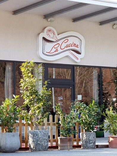 Ein einladendes Restaurant mit dem Namen "La Cucina" und einer Bäckerei. Die Fassade ist von vielen Pflanzen in Töpfen umgeben. | © TV Region Graz - Lunghammer