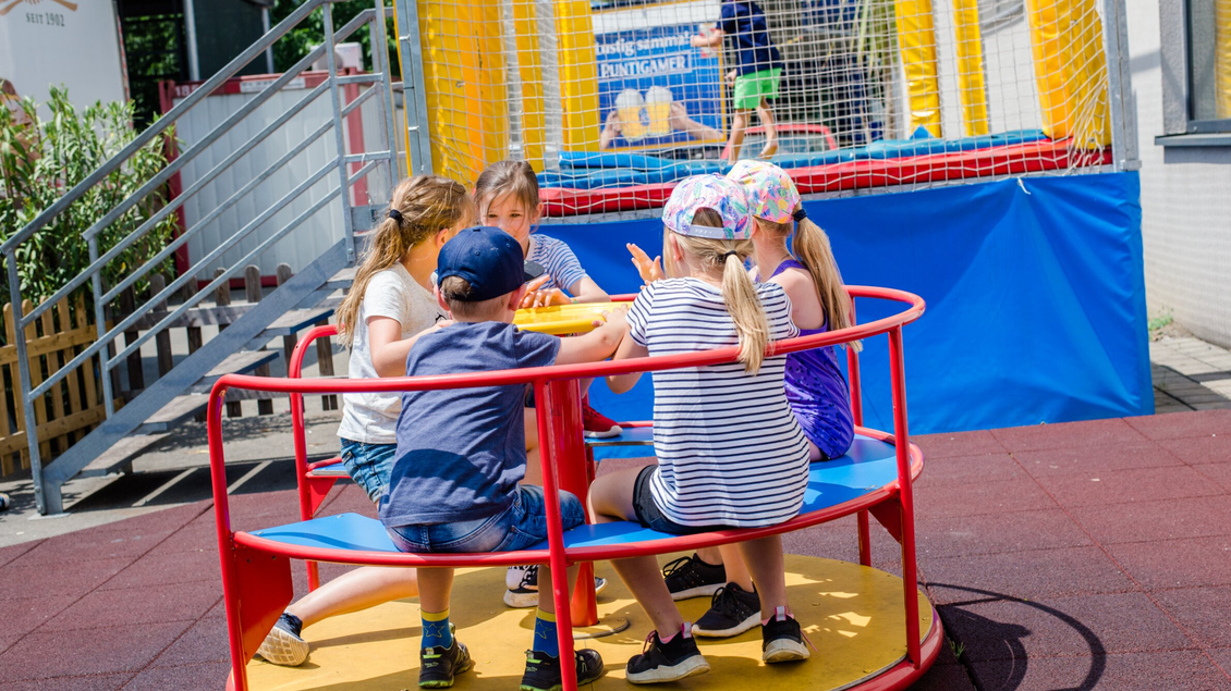 Eine Gruppe von Kindern sitzt auf einem Spielgerät im Freien und spielt zusammen. Im Hintergrund ist eine Hüpfburg sichtbar. | © TV Reigon Graz - Mias Photoart