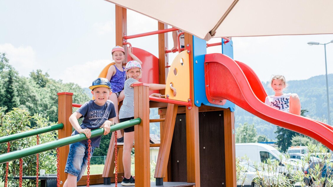 Eine bunte Spielplatzanlage mit einer Rutsche und Klettergerüst. Einige Kinder spielen ausgelassen und haben Spaß. | © TV Region Graz - Mias Photoart