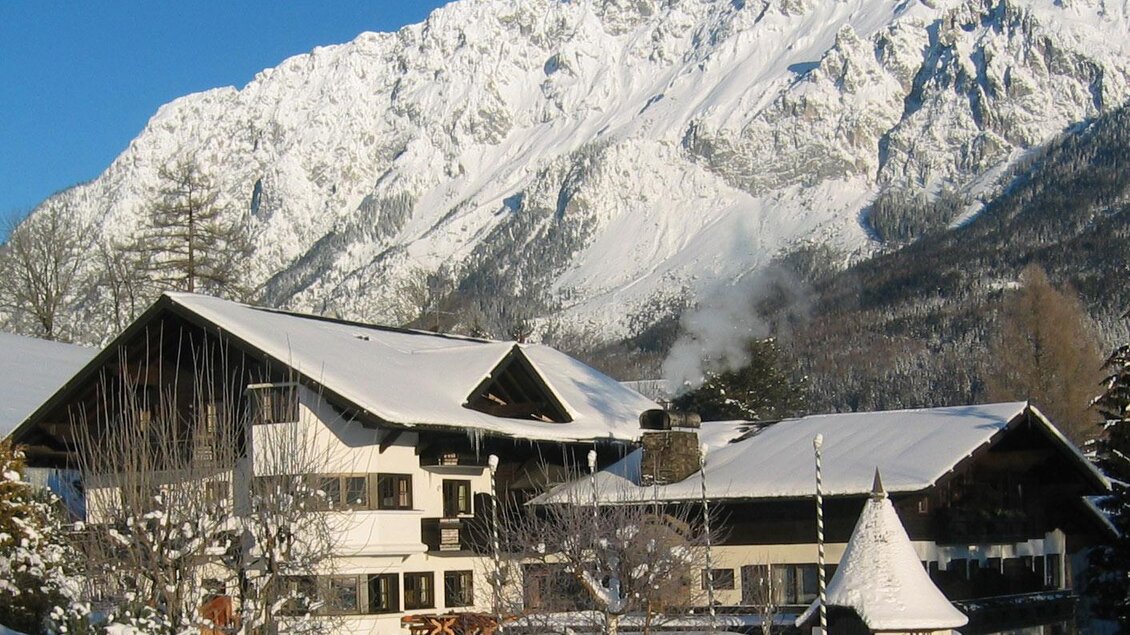 Ein charmantes, schneebedecktes Haus in den Alpen, umgeben von majestätischen Bergen. Der Himmel ist klar und strahlend blau. | © Restaurant Landhaus St. Georg
