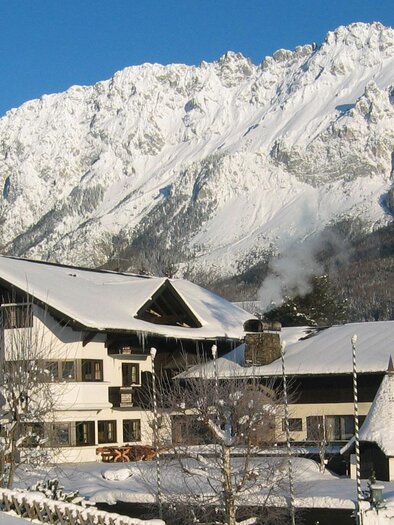 A charming, snow-covered house in the Alps, surrounded by majestic mountains. The sky is clear and brilliantly blue. | © Restaurant Landhaus St. Georg