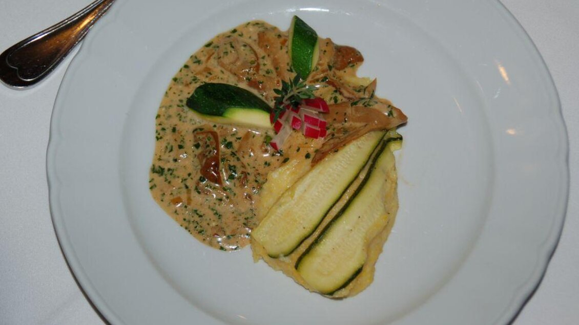 Ein Teller mit einer cremigen Sauce, verfeinert mit Pilzen und frischen Kräutern. Daneben liegen einige Zucchinistreifen und eine kleine Tomaten-Garnitur. | © Restaurant Landhaus St. Georg