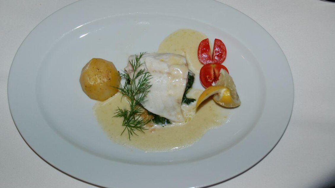 Ein elegant angerichteter Teller mit Fischfilet, Petersilie und einer sahnigen Sauce. Dazu serviert sind Kartoffeln und halbierte Kirschtomaten. | © Restaurant Landhaus St. Georg
