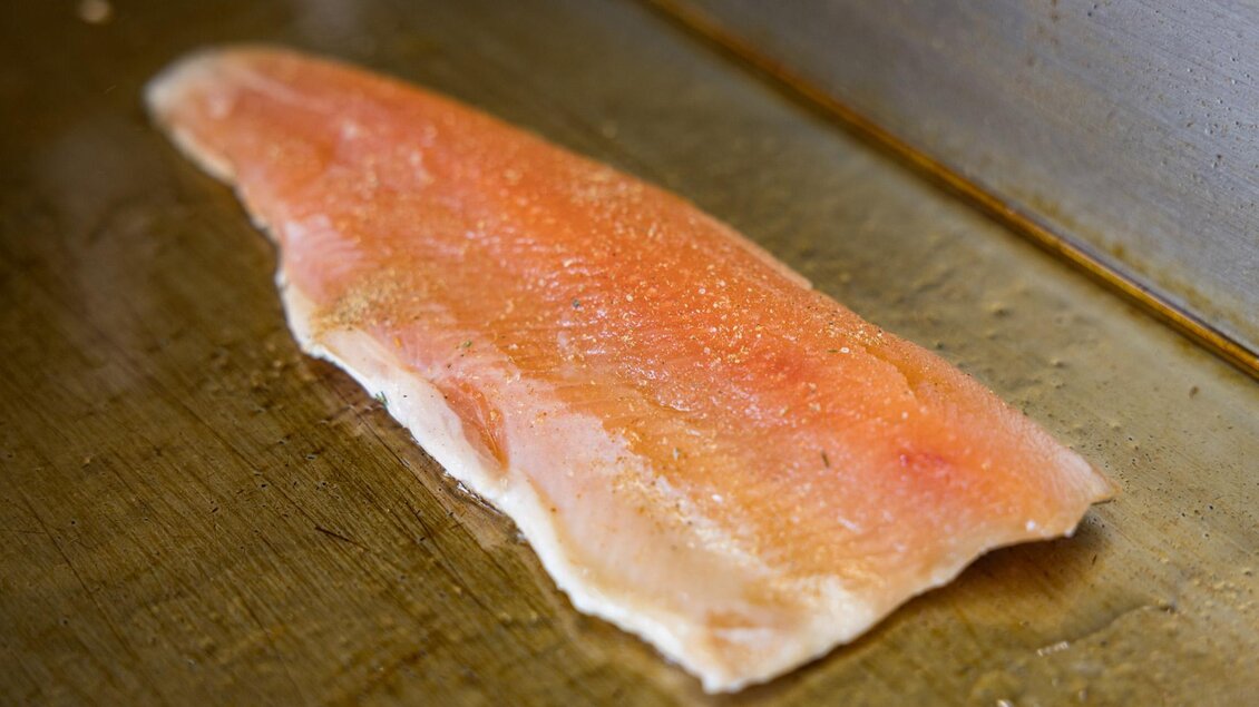 Ein frisches Fischfilet liegt auf einer Grillplatte. Die zarte Textur und die rosa Farbe sind gut sichtbar. | © Netzwerk Kulinarik wildbild