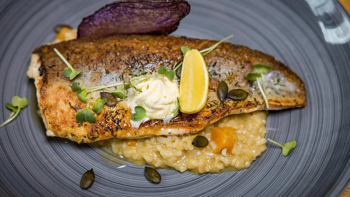 Ein gebratenes Fischfilet auf einem Bett aus Risotto. Garniert mit Zitrone und frischen Kräutern. | © Netzwerk Kulinarik wildbild