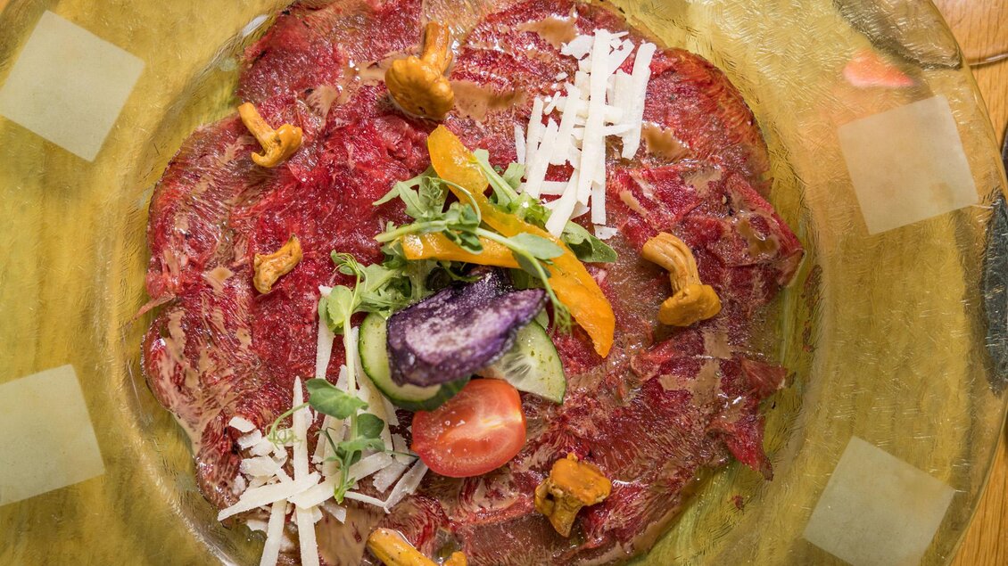 Ein Teller mit Carpaccio, garniert mit frischem Gemüse und Käsespänen. Die Farben der Zutaten verleihen dem Gericht eine appetitliche Präsentation. | © Netzwerk Kulinarik wildbild
