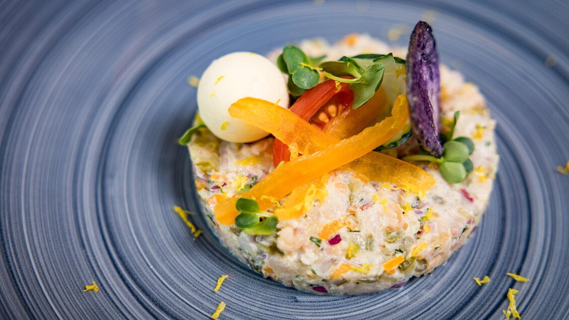 Ein kunstvoll angerichteter Salat auf einem blauen Teller. Er enthält frisches Gemüse, Kräuter und eine kleine Ei-Hälfte als Garnitur. | © Netzwerk Kulinarik wildbild