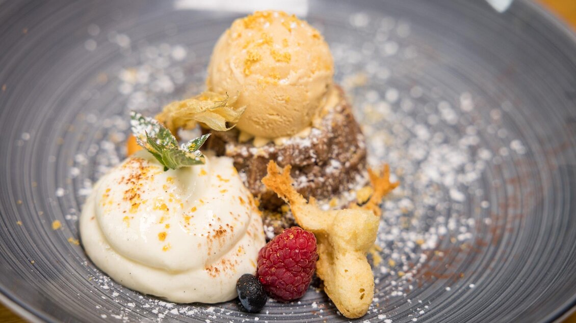 Ein köstliches Dessert mit einem warmen Schokoladenkuchen und einer Kugel Vanilleeis. Dazu gibt es Sahne, frische Beeren und Puderzucker. | © Netzwerk Kulinarik wildbild