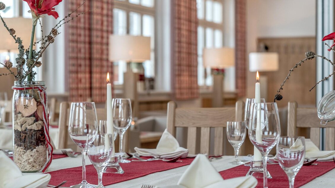 Ein elegant gedeckter Tisch mit Glaswaren und feinem Besteck. Rote Tischläufer und Blumenarrangements sorgen für eine einladende Atmosphäre.