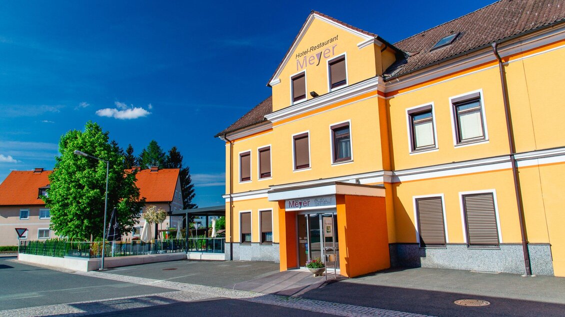 Ein farbenfrohes Restaurant mit gelber Fassade und modernen Fenstern. Die Umgebung ist ruhig mit grünen Bäumen und klar blauem Himmel. | © TV Region Graz - Mias Photoart