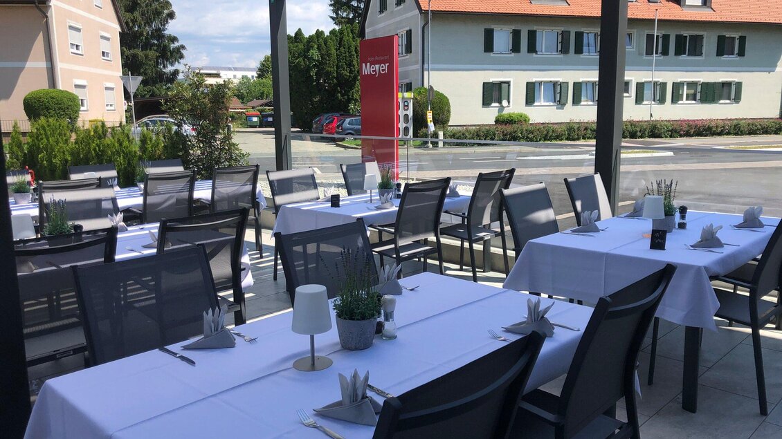 Eine einladende Terrasse mit weißen Tischdecken und Stühlen. Im Hintergrund sind einige Bäume und ein Gebäude zu sehen. | © Jürgen Fuchs