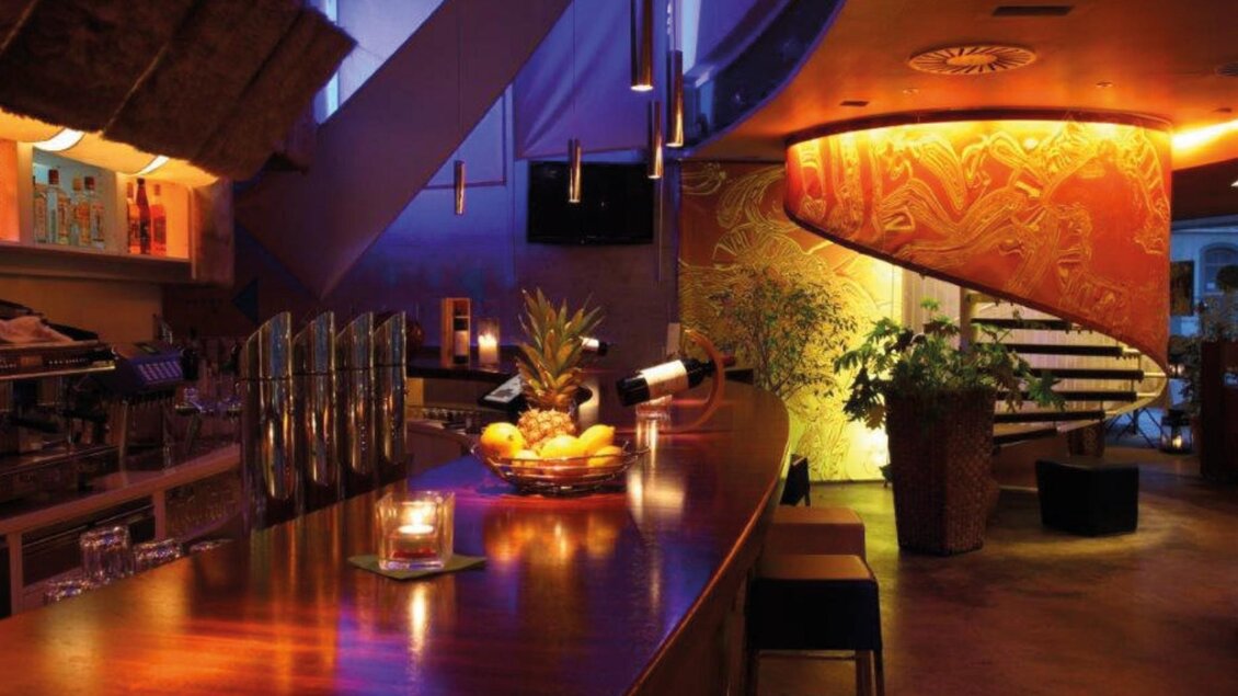 ange Holzbar mit Cocktailshakern, Kerze und Obstschale vor beleuchteter Wendeltreppe. | © Restaurant Rondo