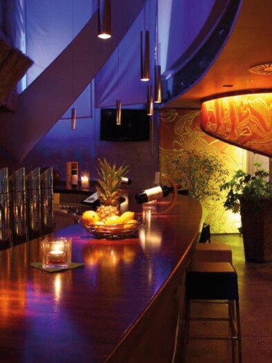 wooden bar with cocktail shakers, candle, and fruit bowl in front of a illuminated spiral staircase. | © Restaurant Rondo