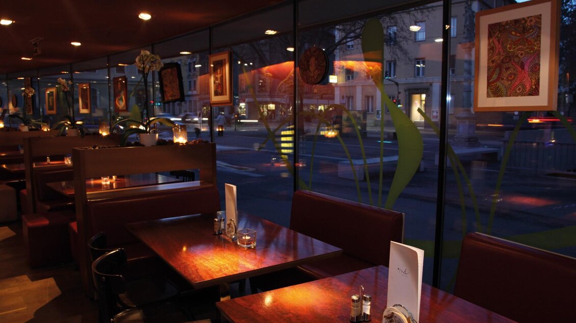 Reihen von Holztischen mit Kerzenlicht vor großer Fensterfront mit Straßenblick. | © Restaurant Rondo