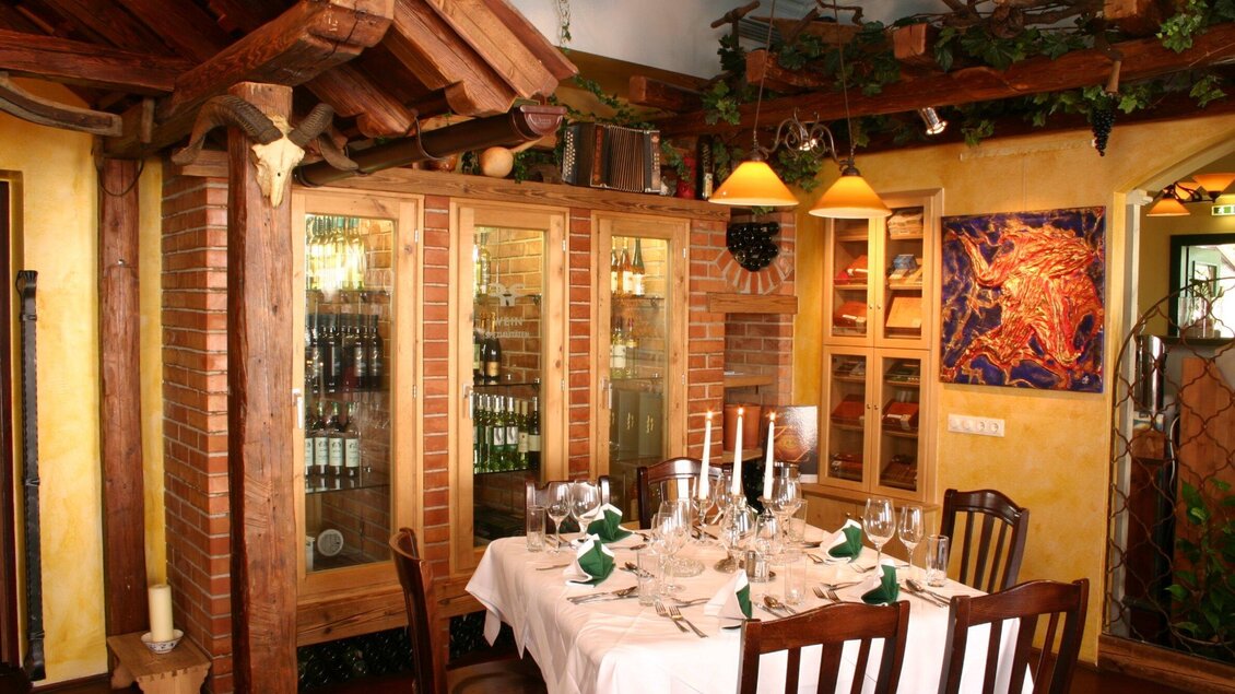 Ein gemütliches Restaurant mit liebevoll gedecktem Tisch. Im Hintergrund befinden sich Regale mit Weinflaschen und kunstvolle Dekoration. | © Rudolf