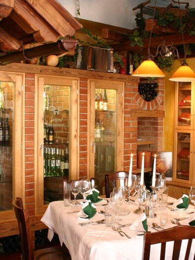A cozy restaurant with a lovingly set table. In the background, there are shelves with wine bottles and artistic decoration. | © Rudolf
