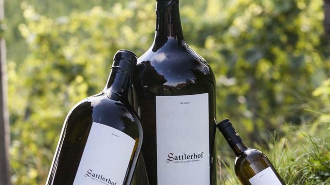 Drei Flaschen Wein stehen auf grünem Gras vor einem Weinberg. Die Flaschen haben unterschiedliche Größen und tragen das Etikett "Sauterhof". | © Sattler