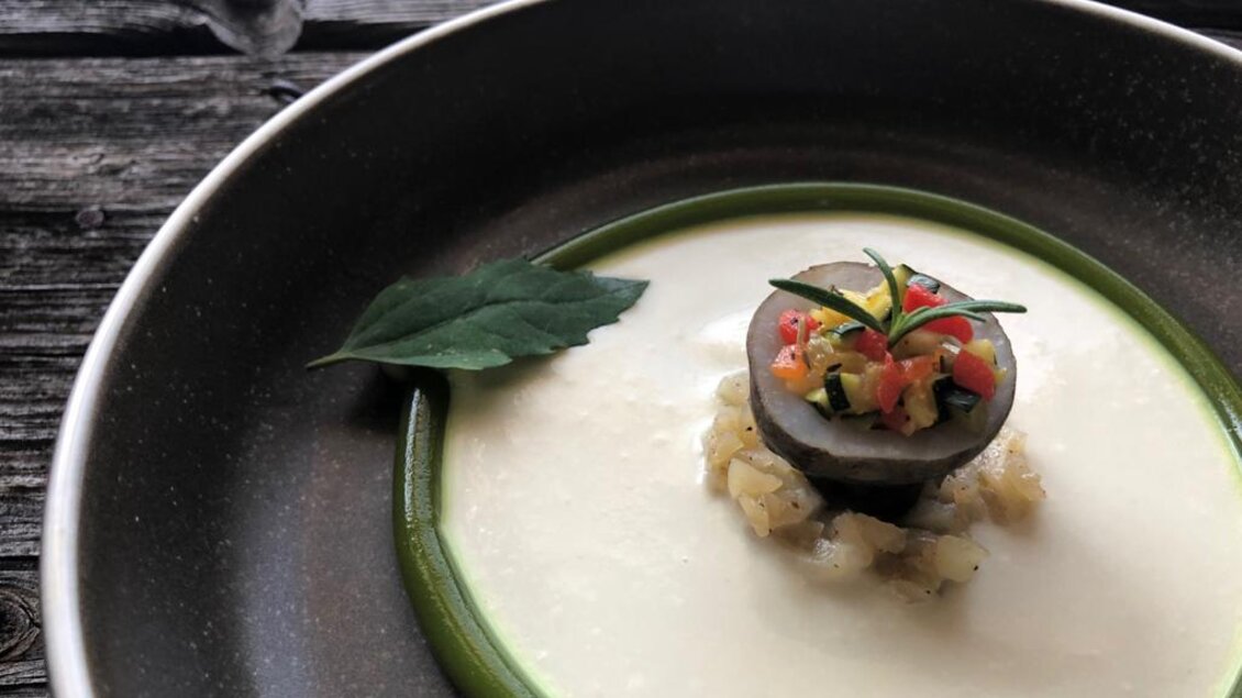 Ein eleganter Teller mit einer cremigen Sauce, dekoriert mit einer runden Komposition aus Gemüse. Frische Kräuter verleihen dem Gericht eine ansprechende Note. | © Sattler
