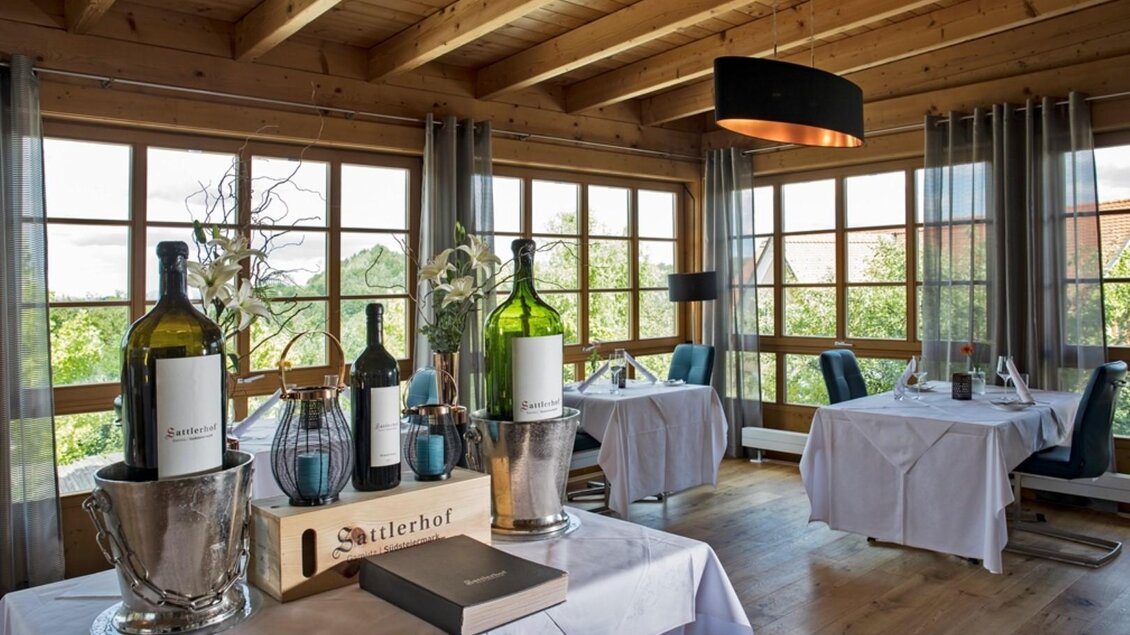 Ein gemütliches Restaurant mit Holzdecke und großen Fenstern. Tische sind elegant gedeckt und mit Weinflaschen dekoriert. | © Sattler
