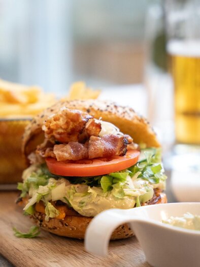Burger mit Gemüse und Speck, dazu Pommes und ein Bier auf einem Holztisch im Schachenwald | © Schachenwald - Wolfgang Hummer