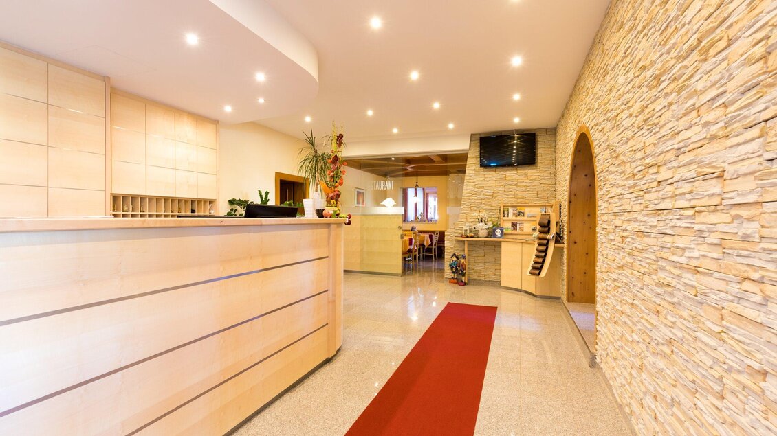 Eine moderne Lobby mit einem Empfangstresen aus Holz und einer einladenden Atmosphäre. Die Wände sind mit hellem Stein verkleidet und es gibt einen roten Teppich, der den Raum akzentuiert. | © Region Graz - Harry Schiffer