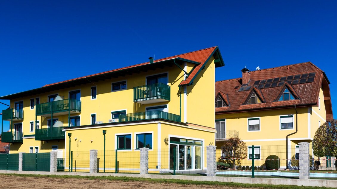 Gelbe Gebäude vom Schachenwald mit Balkonen, Gartenbereich und blauem Himmel. | © Region Graz - Harry Schiffer